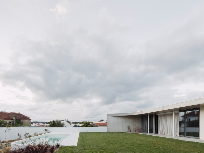 Rooftop lawn and pool terrace with curved concrete volume wrapping glass doors under overcast clouds