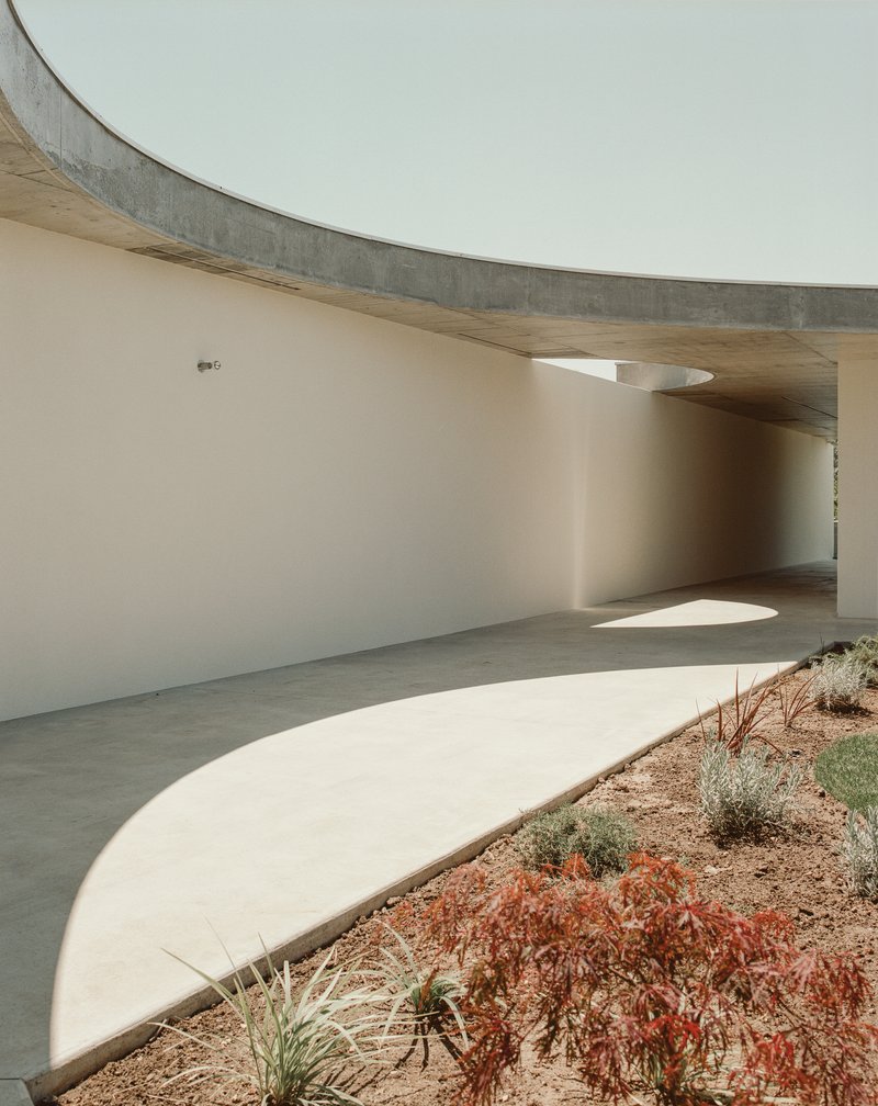 Curving passage beneath board-formed concrete soffit with circular roof openings casting light pools