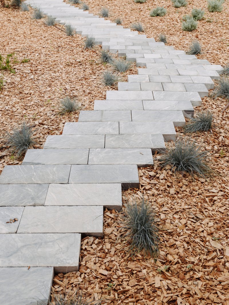 Stone paver pathway zigzagging through gravel mulch and low grasses in a dry landscape