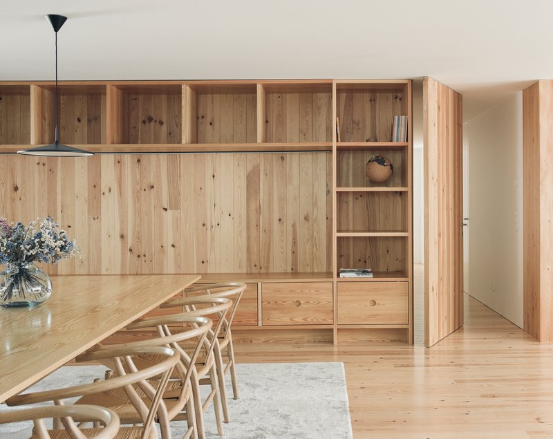 Dining area with timber storage wall, open shelving, and chairs around a long table