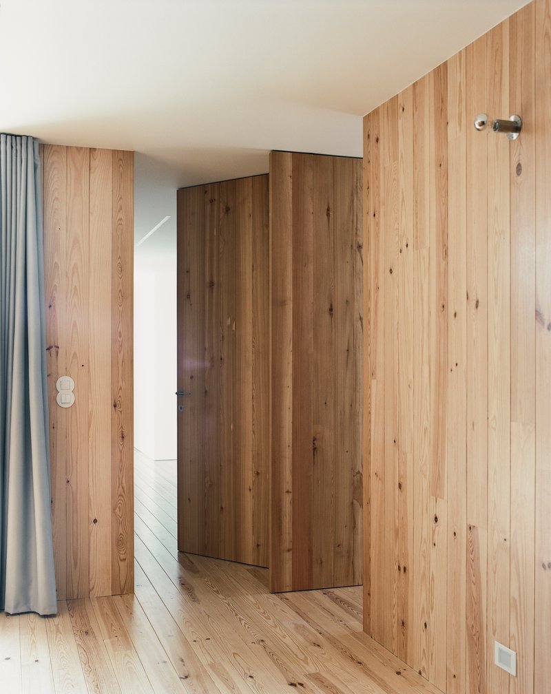 Vertical timber wall panels concealing a door beside a grey curtain under soft daylight