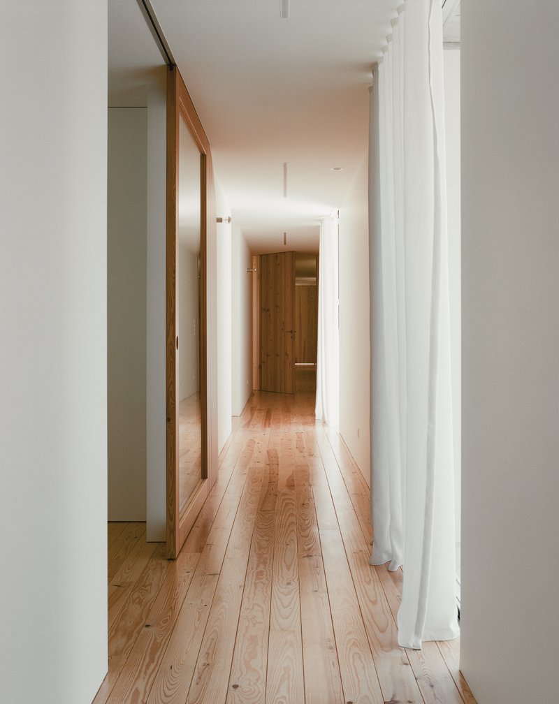White hallway with timber sliding door and oak flooring lit by recessed ceiling fixtures