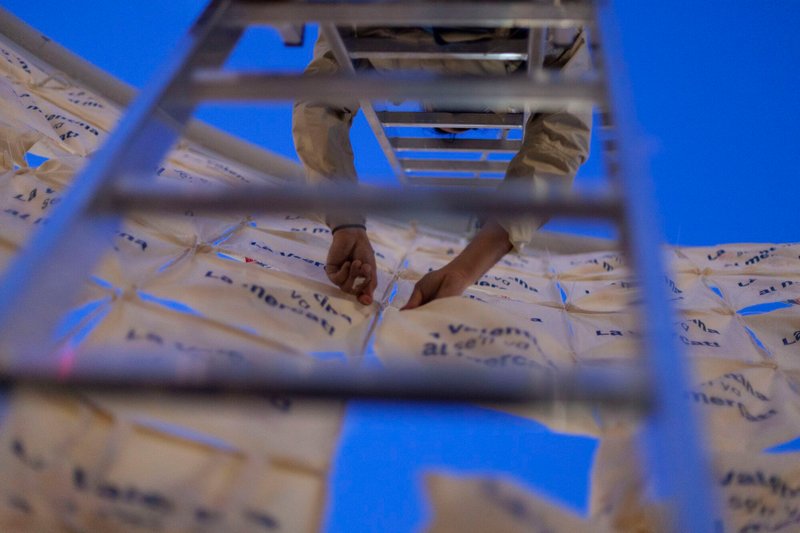 View through white frame grid showing hands binding printed fabric panels together