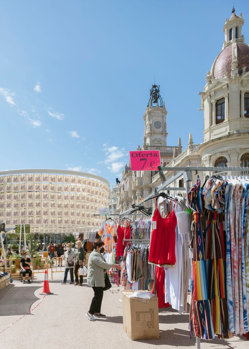 Temporary pavilion with repeating textile screen beside clothing racks in a public plaza