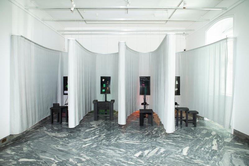 Exhibition space with curved white curtain partitions and swirling grey marble floor under track lighting