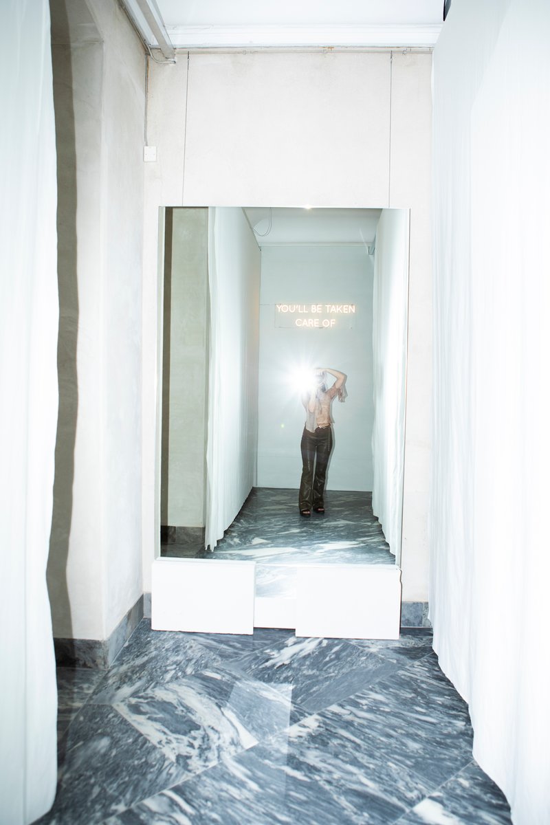 Narrow corridor with white walls and marbled grey flooring leading to a small exhibition alcove