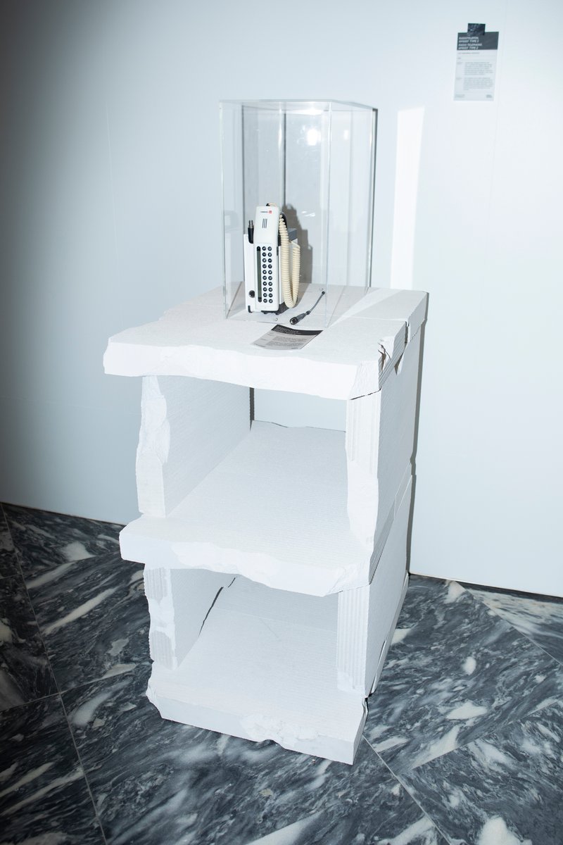 White tiered display stand with architectural models and remote control on dark marbled floor