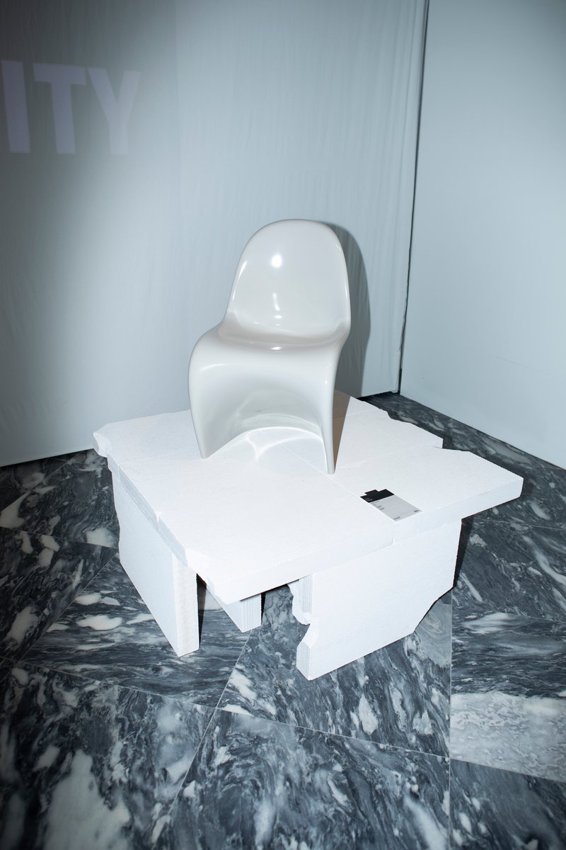 White molded chair and geometric table on swirling dark marble flooring near pale curtain