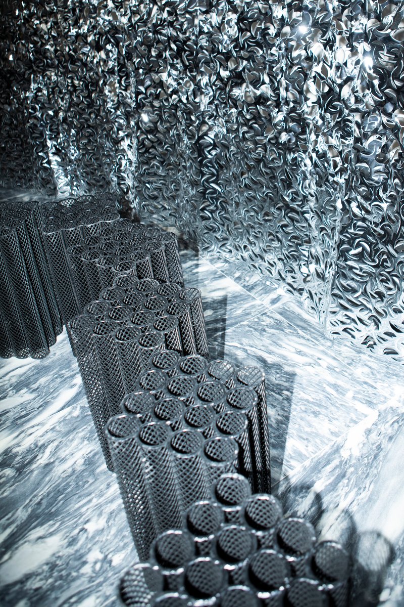 Textured black mesh staircase ascending through reflective metallic chain-link wall surface