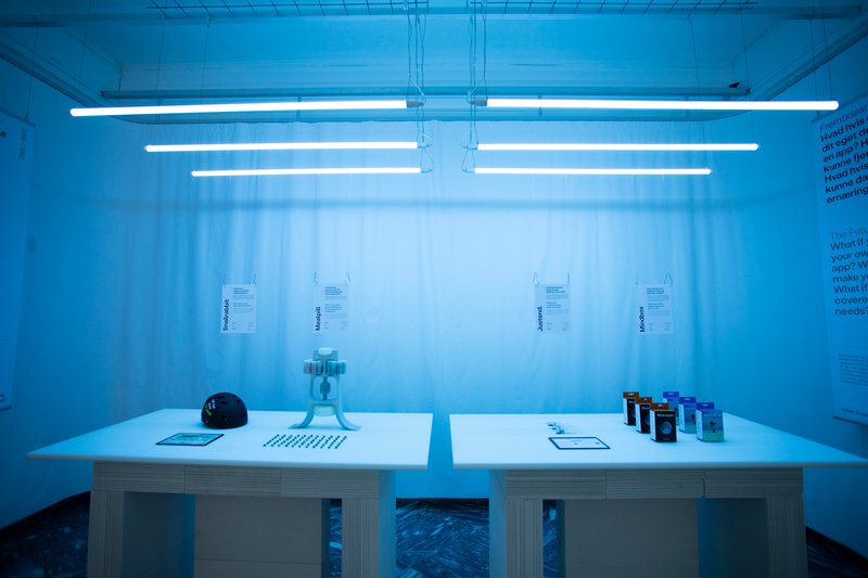White display table with material samples beneath fluorescent tube lighting and sheer curtain backdrop