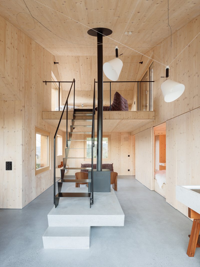 Double-height interior with central black stove pipe and steel staircase leading to sleeping loft above