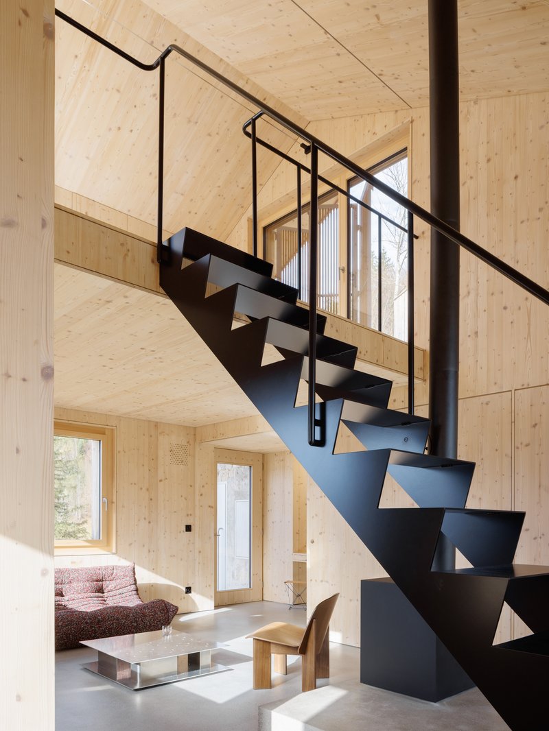 Folded steel staircase with triangular cutout treads and tubular handrail against pale plywood walls