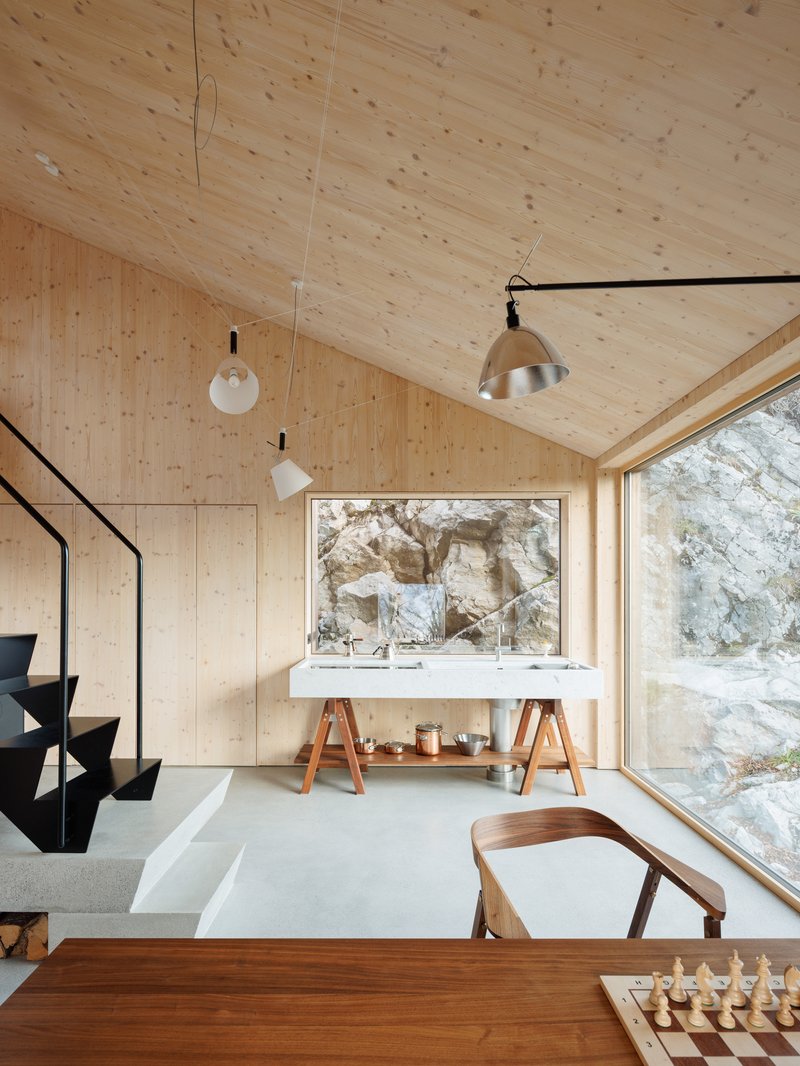Living area with pale timber walls and ceiling, suspended pendants, and floor-to-ceiling window overlooking rocky terrain