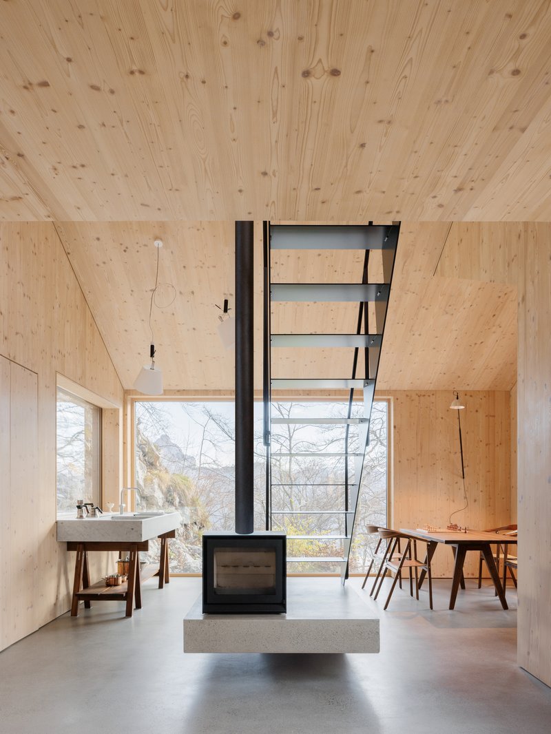 Central freestanding woodstove with black flue pipe beneath a plywood ceiling in the open living space
