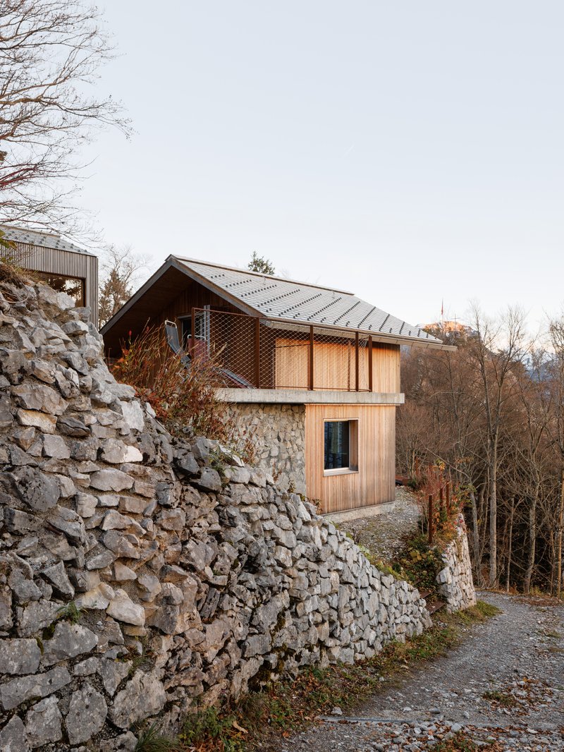 Timber-clad dwelling with metal roof perched above a dry stone retaining wall in late autumn