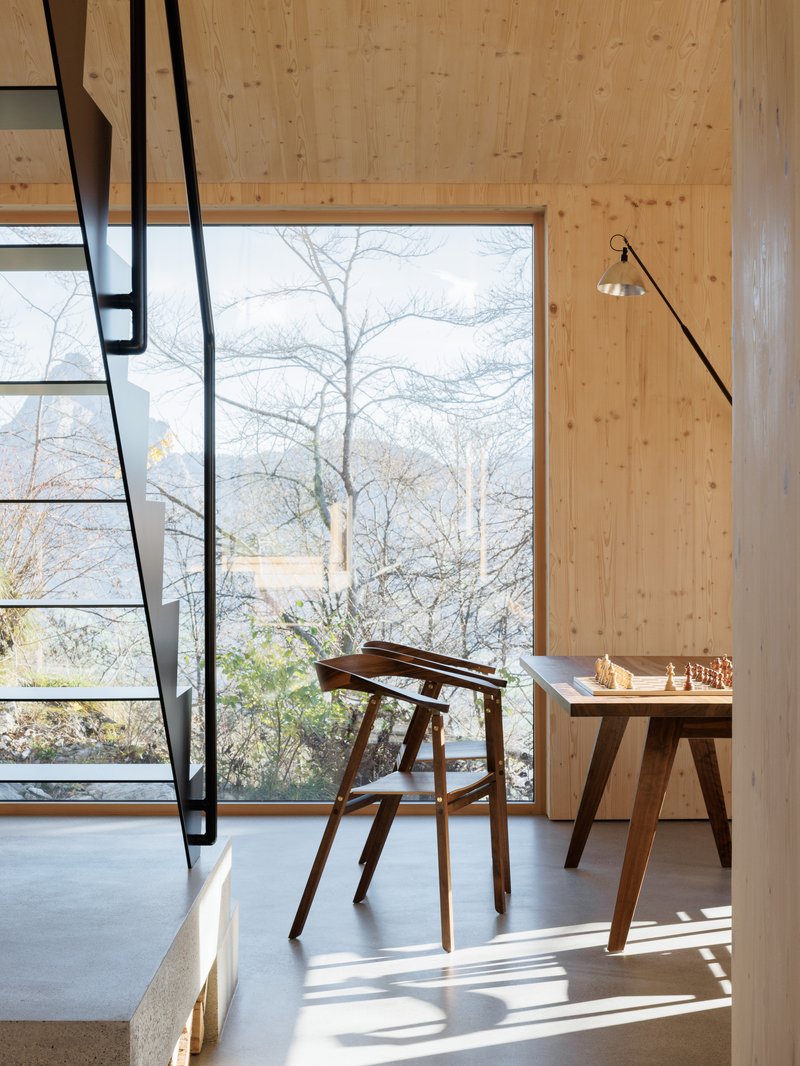 Interior with black steel staircase, timber wall paneling, full-height window framing bare winter trees