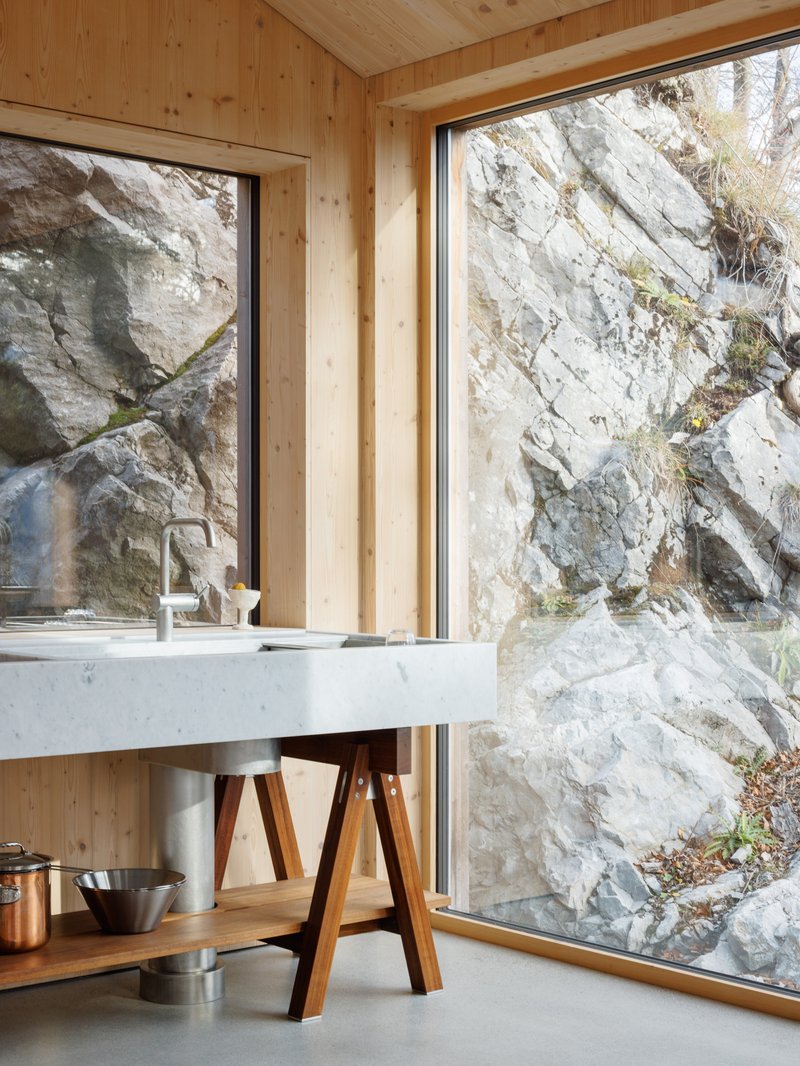 Kitchen sink on timber trestles facing floor-to-ceiling windows with exposed rock face beyond