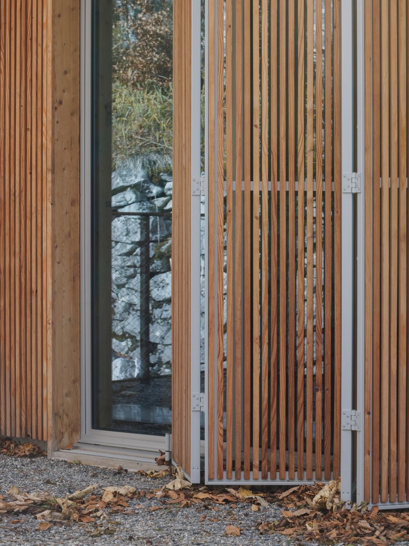 Vertical timber slat screen sliding open on a steel frame with gravel ground and fallen autumn leaves