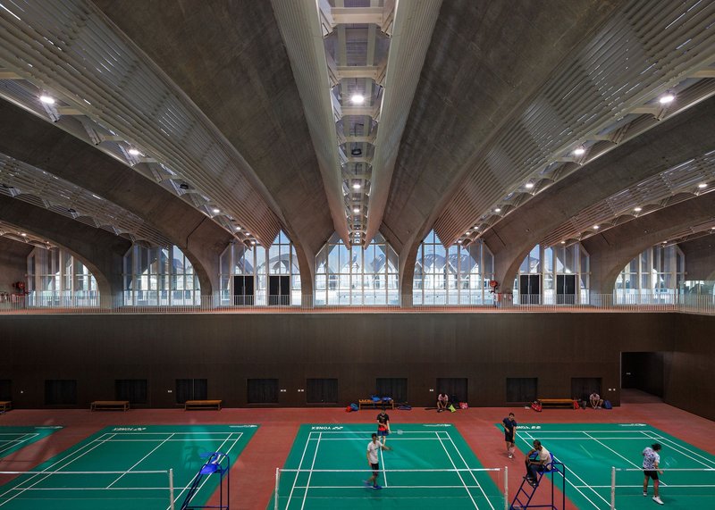 Interior sports hall with badminton courts under ribbed concrete vaults and clerestory windows