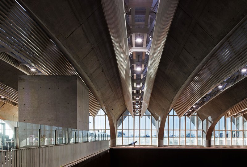 Interior view showing concrete vaulted ceiling with integrated lighting and arched glazed wall beyond mezzanine