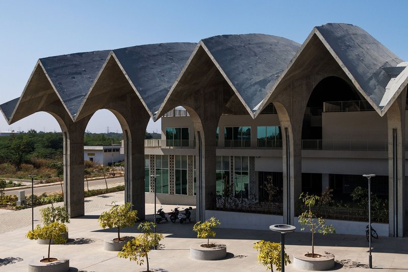 Covered plaza beneath the arched concrete canopy with young trees in circular planters