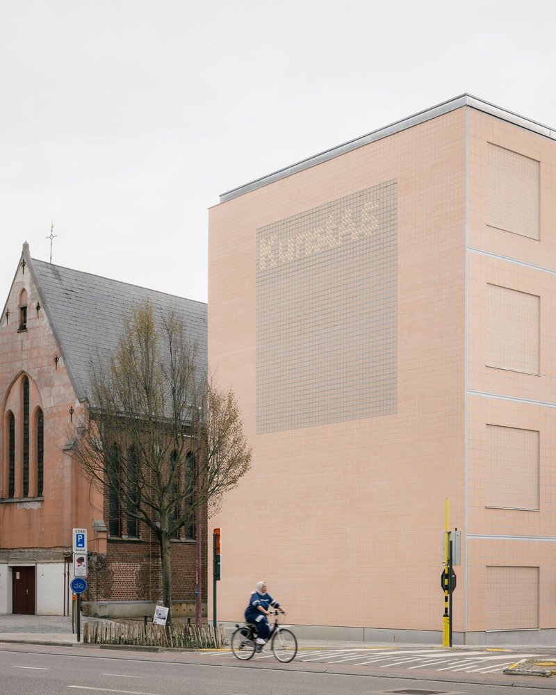 Street view of peach brick facade with gridded glass block window alongside a cyclist passing a church
