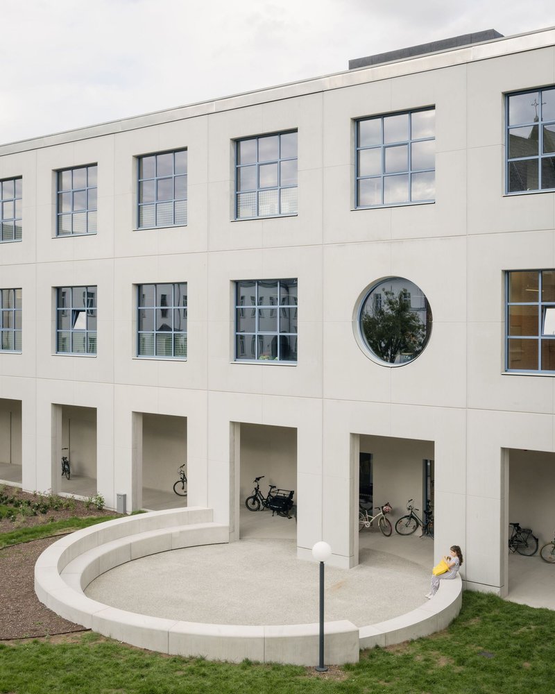 Courtyard with circular seating plinth and open bicycle storage bays beneath gridded windows