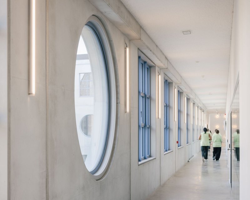 Corridor with oval window and vertical tube lights alongside two figures walking