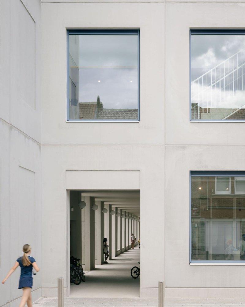 White facade opening framing the colonnade with a woman walking past in afternoon light