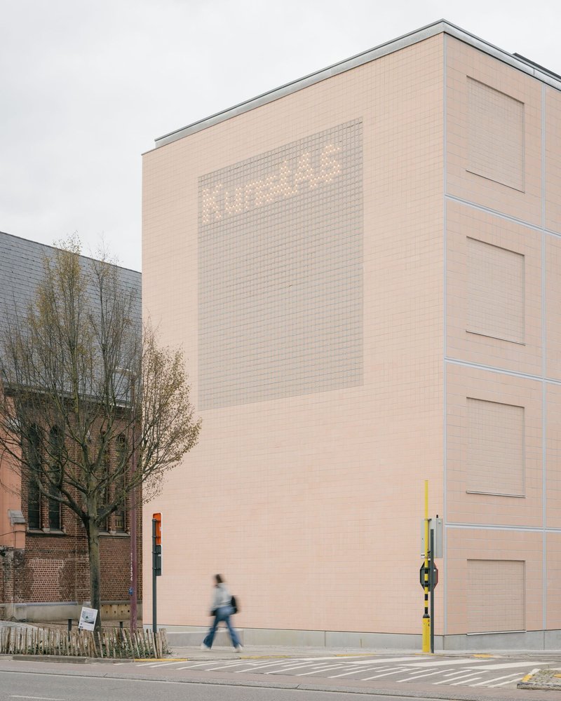 Tall tiled facade with backlit translucent panel and a pedestrian crossing the street