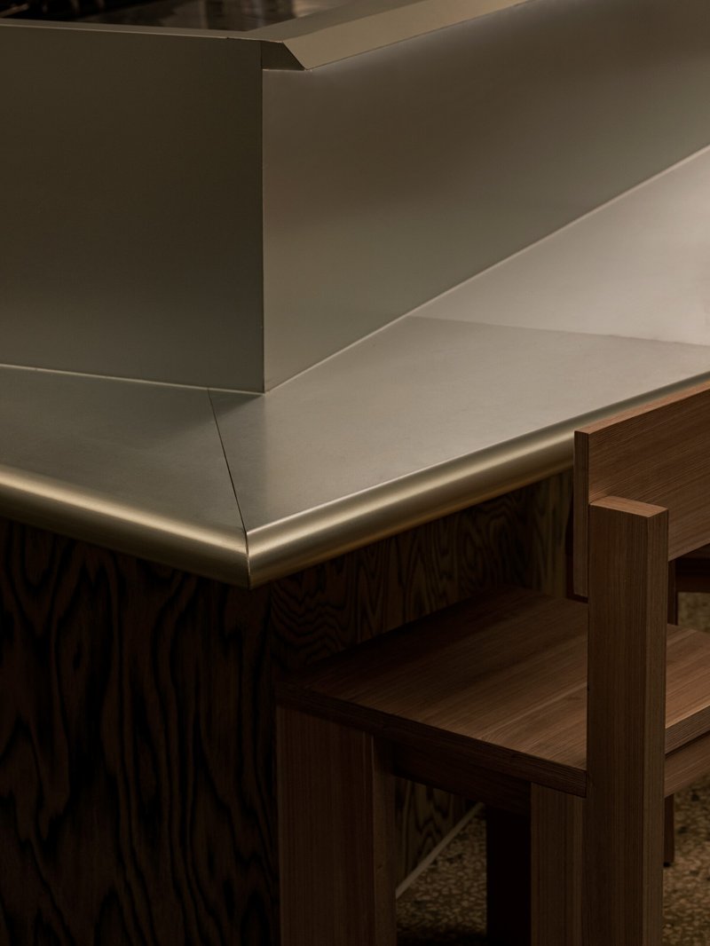 Detail of brushed brass counter edge meeting timber millwork beneath white plaster walls