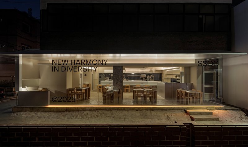 Street view through full-height glass storefront showing dining room interior at dusk