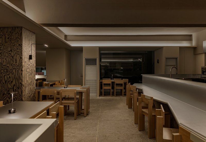 Interior view across terrazzo flooring showing timber seating and wood-paneled column at night