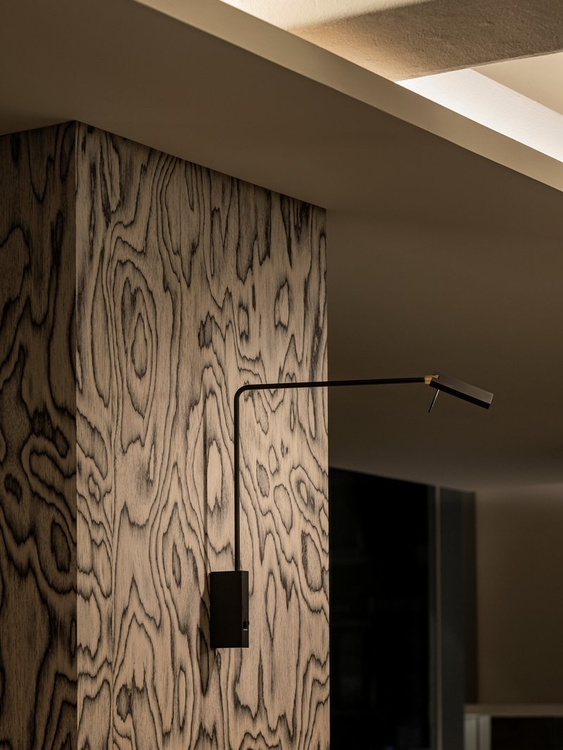 Figured wood grain wall panel with black swing-arm wall sconce in recessed ceiling