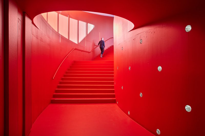 Red-painted staircase curving upward through a cylindrical void with a person ascending midway