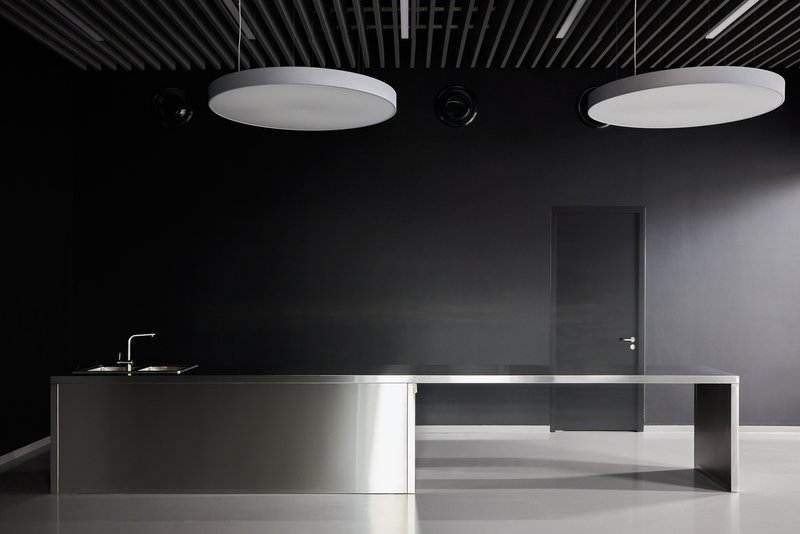 Minimalist kitchen island with stainless steel base and integrated sink beneath two circular ceiling fixtures