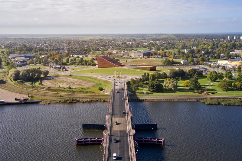 Aerial perspective showing the folded copper roof beyond a pedestrian bridge crossing the river in autumn