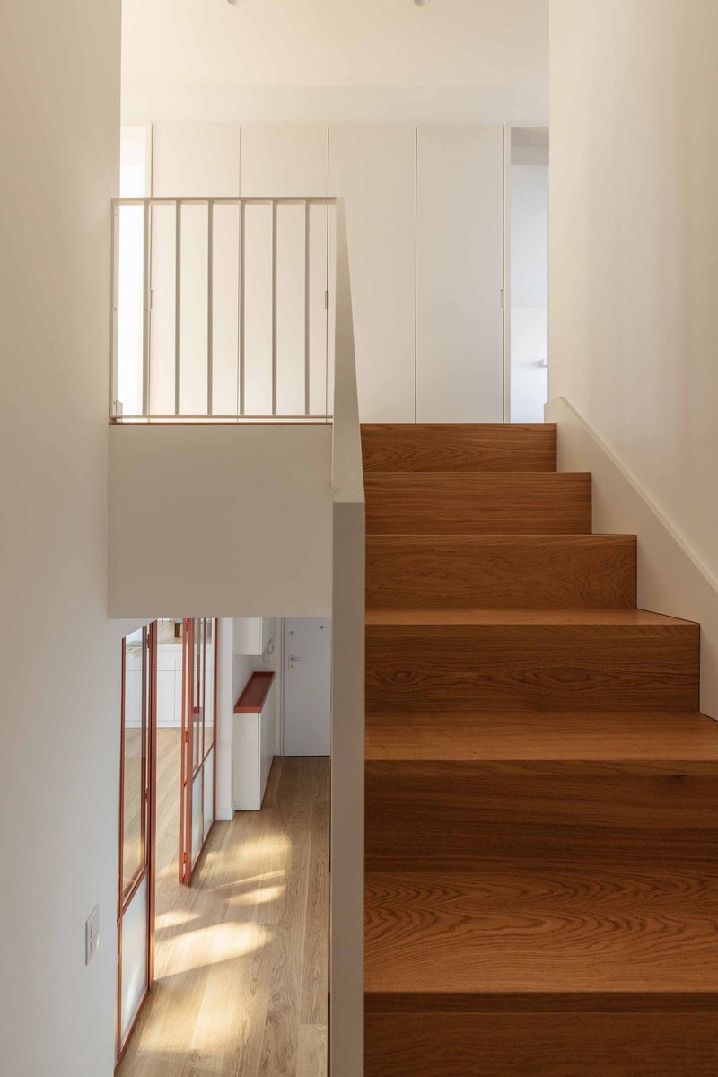 Timber staircase with vertical balustrade overlooking hallway with sunlight streaming through windows
