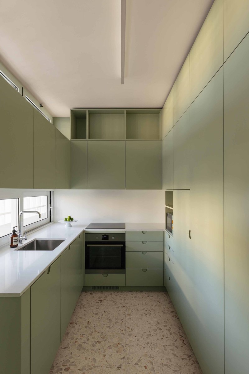 Compact kitchen with sage green cabinetry, white countertops and terrazzo flooring
