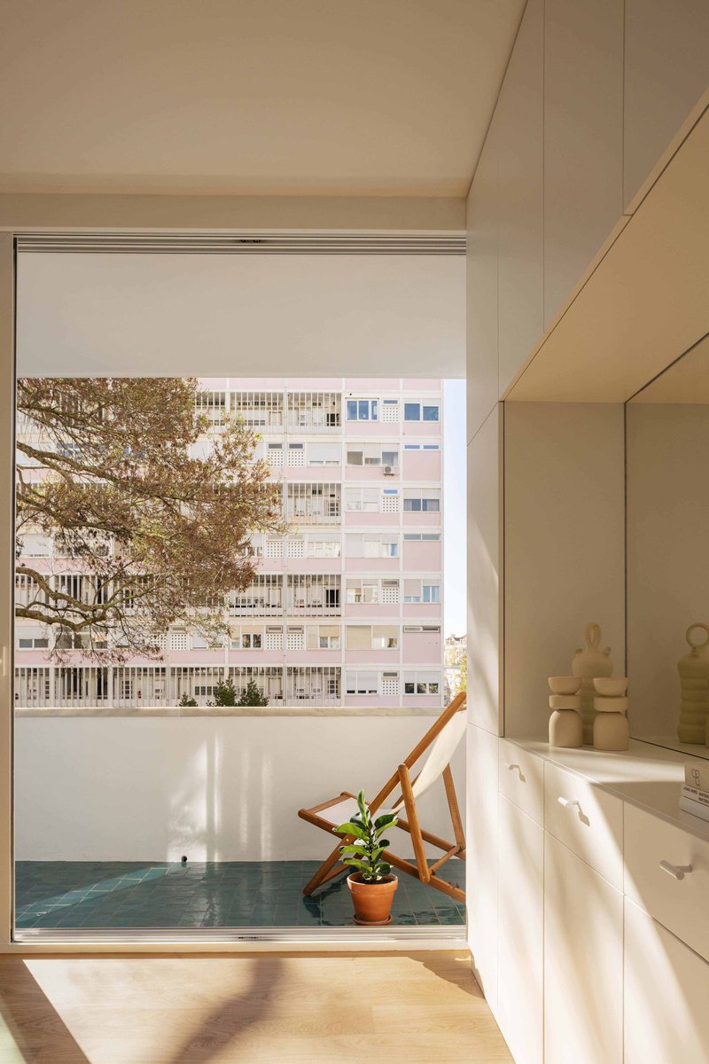 Window seat with teal cushion and potted plant overlooking residential buildings