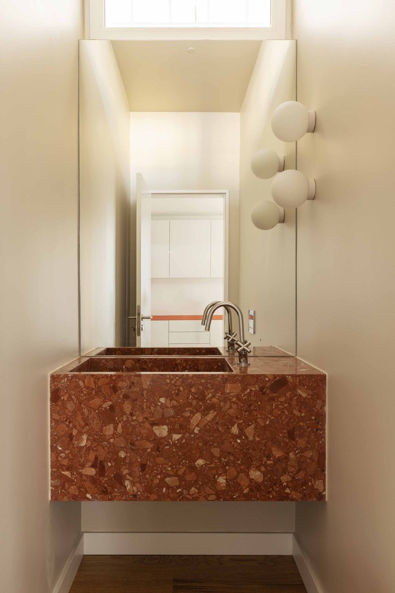 Red terrazzo basin with integrated counter and polished brass faucet in a narrow powder room