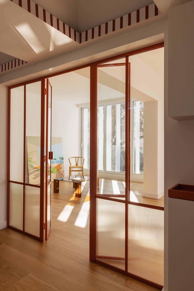 Timber-framed glass doors opening to a sunlit room with wishbone chair visible beyond