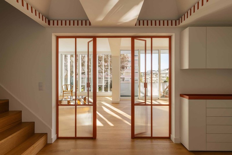 Red-framed folding glass doors opening to a terrace with striped ceiling trim and natural light