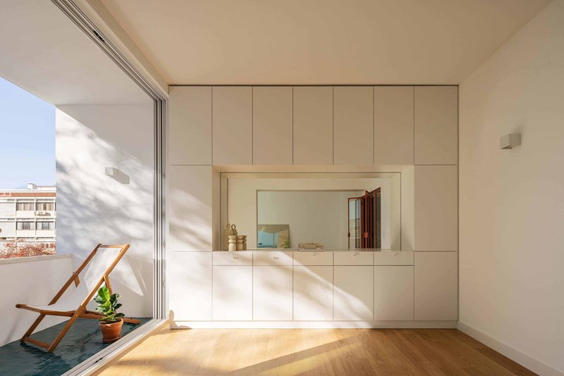 White storage wall with recessed mirror and sliding terrace door opening to a deck chair