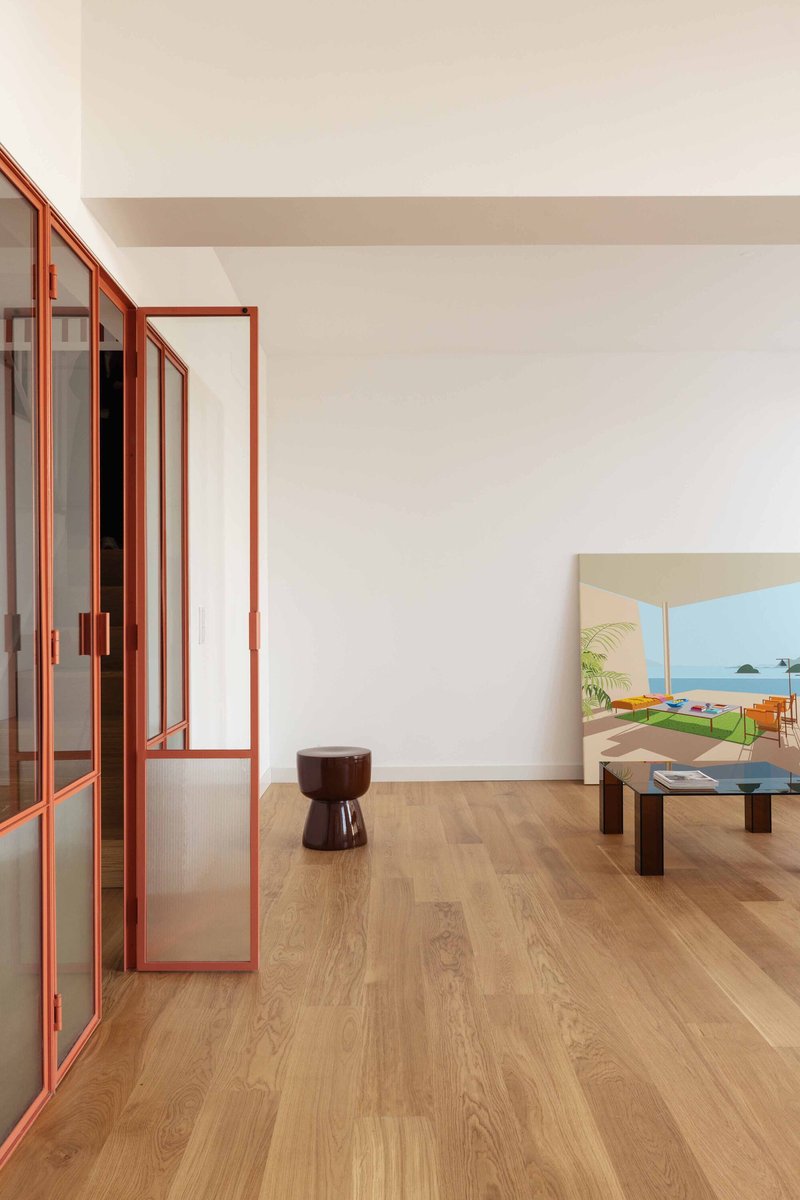 Red-framed partition doors along oak flooring with a coastal painting on the wall