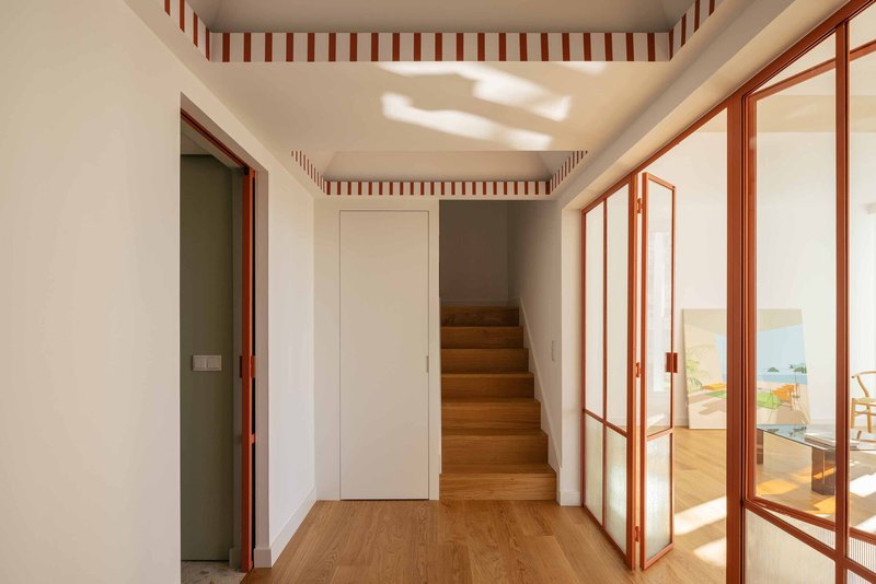 View from hallway through open red-framed doors to a sunlit room with ocean painting