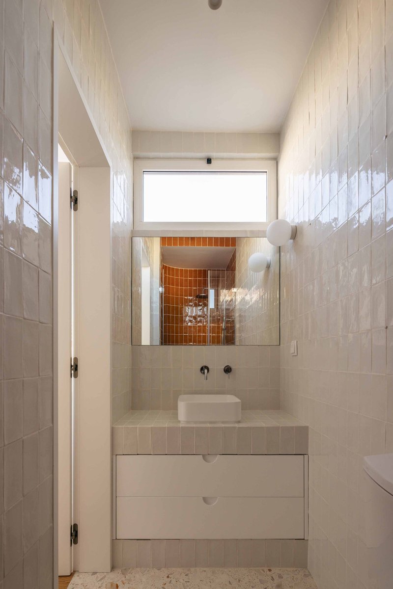 Bathroom vanity with white tile walls and mirror reflecting orange tiled shower niche