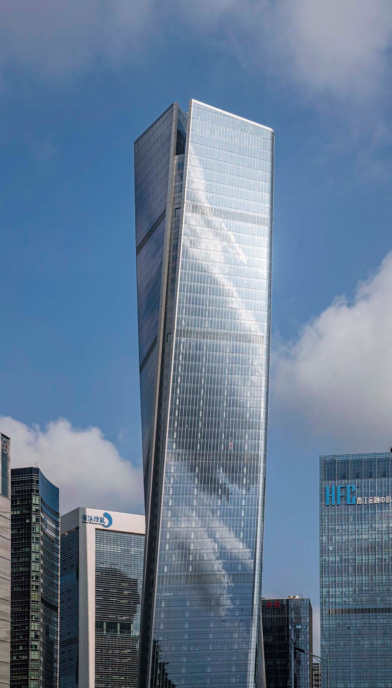 Angled facade of the glass tower showing diagonal structural bracing pattern against passing clouds