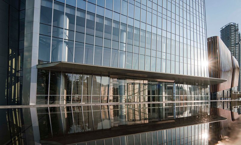 Reflecting pool mirroring the glass curtain wall and elevated pedestrian bridge at the tower base