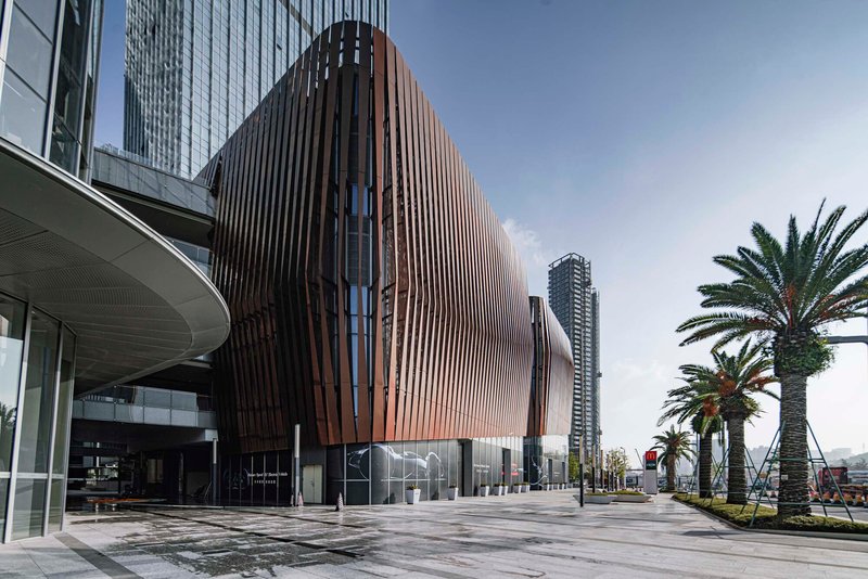 The bulging facade with vertical bronze louvers next to the recessed glass entry and planted palms